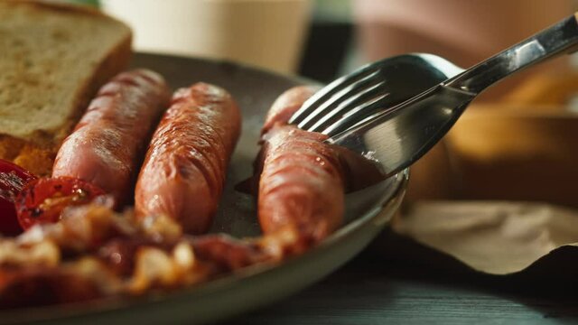 Traditional full English breakfast close-up. National British cuisine, fried eggs with bacon, toasts on plate, eating sausage using fork and kinfe. American pub or cafe, fast food. 