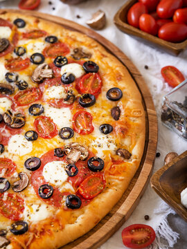 Large Italian pizza on a wooden plate. Beautifully decorated with tomatoes, cheese, olive slices. Macro photography. Color image. High angle view. Restaurant, hotel, pizzeria, fast food.