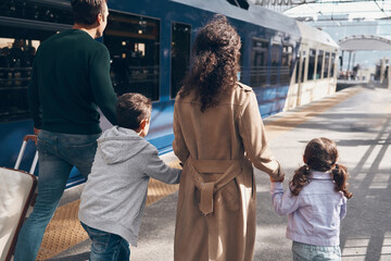 Rear view of family with two little kids walking by railroad station platform together