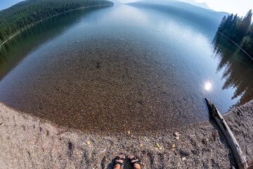 Unique, fisheye wide angle view of Bowman Lake in Glacier National Park, with woman's feet with...