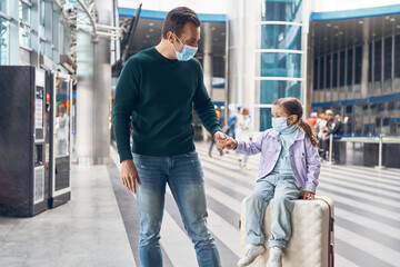 Young father and daughter in protective face masks waiting for boarding in airport terminal