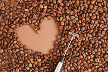 heart made of coffee beans and metal handheld milk steamer on brown background. Handheld frother