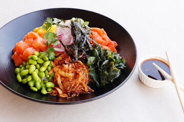 japanese poke bowl with edamame, salmon, wakame seaweed, mango, radish, cucumber, onion and rice served with sweet soy sauce