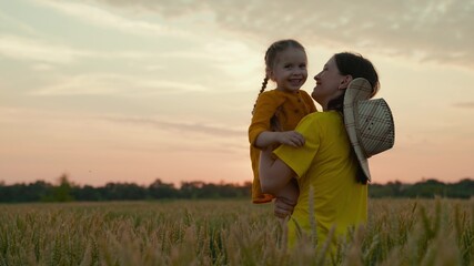 A kind farmer mother with a child in a field with wheat at sunset, growing grain for making bread, a happy child, a family business on a ranch, examining the grown crops with a baby in her arms