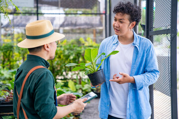 Asian man plant shop owner help customer choosing potted plants in greenhouse garden. Handsome male buying plant and flower for growing at home. Small business and indoor activity lifestyle concept