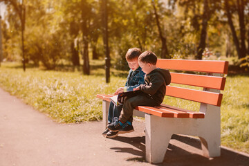 Fototapeta premium Autumn September, two boys reading a book on a park bench, warm, golden autumn