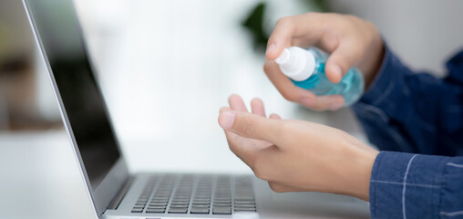 Hand of man work from home with alcohol gel or sanitizer for cleaning hand and protect coronavirus or covid-19, new normal, quarantine and social distancing, businessman using laptop computer.