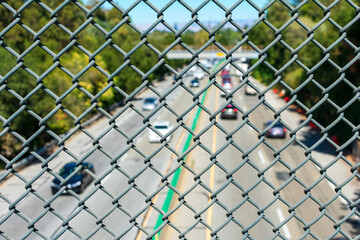 View of blurry highway traffic seen through chain link fence from overpass