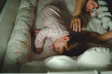 Small caucasian baby going to sleep hands of unknown woman mother putting blanket to cover her...