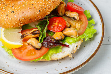 Sandwich with salad leaves, tomatoes and mussels, and cream cheese, on a sesame bun. Close-up