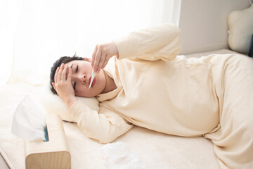 A young pregnant Asian woman lying down and checking thermometer