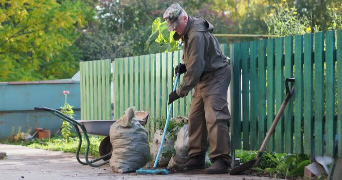 Cleaning. A Man Sweeps The Sidewalk With A Brush, There Are Filled Garbage Bags Nearby. Siberia.