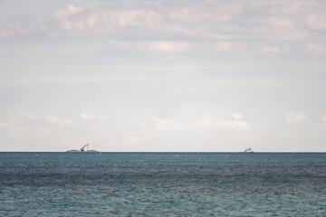 A barge carrying an construction equipment and excavator with piles of stone on either side  floats across the water of Lake Michigan at the horizon being pulled by a tug boat far in the distance.