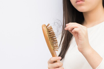 Young woman's hair falls out as she brushes it with the comb due to hair lost.