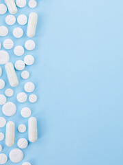 Border of White assorted scattered Medical Pills, tablets, casules On Blue Background With Copy Space. Top view flat lay. Medicine, treatment, health care Creativity Concept. Vertical