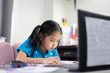 Asian child student or kid girl reading on book to learning and studying online class on computer notebook or person learn from home by video call on laptop for back to school by homeschool education