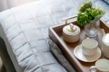 close up wooden tea tray and glass flower vase decoration on soft white bed at bedroom with soft sun light morning weekend vacation