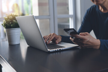 Casual business man using mobile phone and working on laptop computer at home office, work from home concept