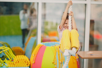 Kids doing exercises climbing tightrope in gym at kindergarten or elementary school. Children sport and fitness concept