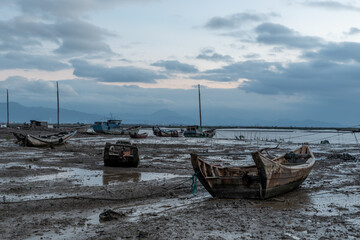 In the shallow area before sunrise in the morning, there are cloudy clouds and many fishing boats on the beach
