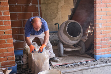 Construction worker opening sandbags to loads a concrete mixer.