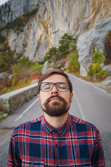 Male hipster Traveler with backpack in plaid shirt and jeans hiking in the mountains travel, trekking in autumn countryside, road in the mountains