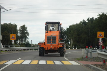 Big heavy 3-axle orange wheeled bulldozer tractor drive after the pedestrian crossing before the railway crossing at summer day, industrial machine traffic on the road
