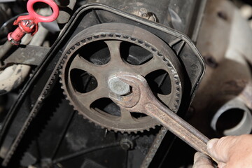 Serviceman hands unscrews with rusty wrench the SOHC camshaft drive gear cogwheel with timing belt on old car motor front face under cover close up under cap of old car