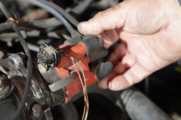 mechanic's hand holding ignition distributor cap with wires on old used car engine, ignition system...
