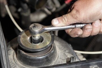Service man hand unscrews the shock absorber nut with wrench closeup under cap hood -   car...