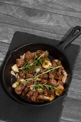 Diced Aberdeen Angus beef with shallots and rosemary, fried in a cast iron frying pan.  Selective colour image