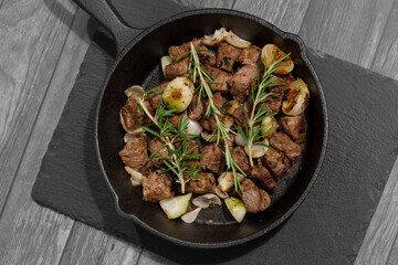 Diced Aberdeen Angus beef with shallots and rosemary, fried in a cast iron frying pan.  Selective colour image