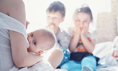 Maternity concept. A young mother feeds her little baby. First lure and breastfeeding. Family in white clothes.
