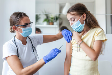 Doctor vaccinating girl. Injecting COVID-19 vaccine into patient's arm. Girl in medical masks...