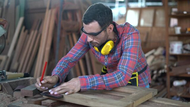 carpenter wearing Safety Glasses and Protective ear muffs measure distance with a pencil and a corner ruler wood  in workshop .craftsman Mark point to cutting on plank