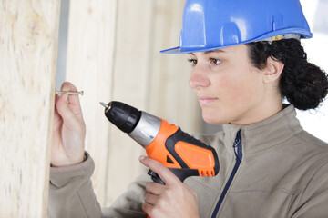 female builder using cordless screwdiver to insert screw in wall