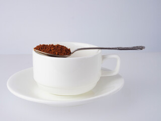 Spoon of instant coffee granules above white cup and saucer