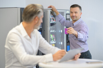 businessman offering colleague a drink from vending machine