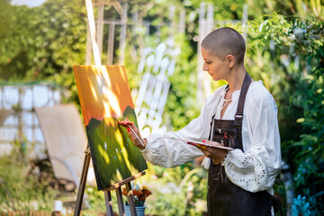 Beautiful young woman relaxing while painting an art canvas outdoors in her garden. Cancer...