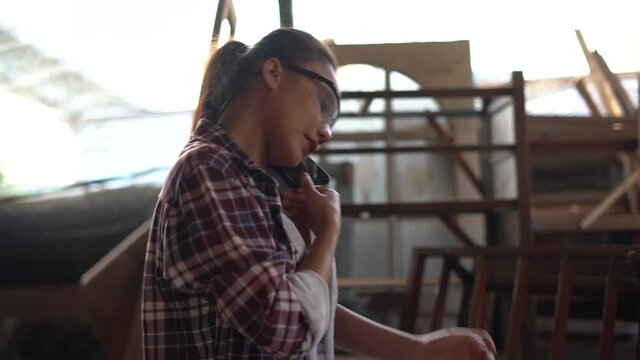 young asian business woman talking on phone making order on tablet in wood working factory . female carpenter working in her workshop