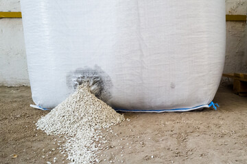 Leakage of granular mineral fertilizers through a hole punched in a jumbo bag inside a warehouse. Defective, leaky bag with ammonium sulfate in stock