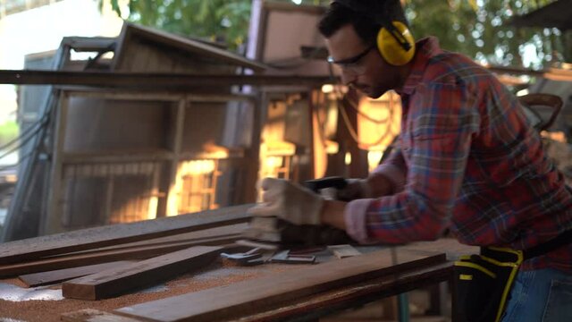carpenter wearing Safety Glasses and Protective ear muffs using electric wood plane with plank  in wood working factory