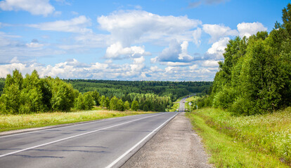 Straight road with a marking on the nature background. Open Road in future, no cars, auto on asphalt road through green forest, trees. Clouds on blue sky in summer, sunshine, sunny day. Bottom view