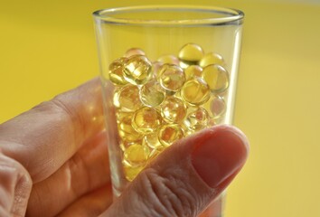 pills capsules oil in glass cup in hand beautiful texture yellow background