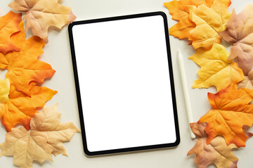 close up top view mockup of white  blank digital tablet screen and stylus pen with group of dried orange color maple leaves background texture or autumn season collection design concept