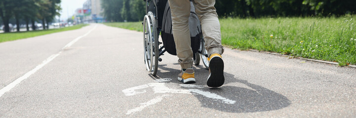 Fototapeta premium Man helping disabled person in wheelchair to walk on sidewalk