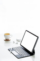 Blank screen tablet with magic keyboard, coffee cup and earphone on whilte background, vertical view.