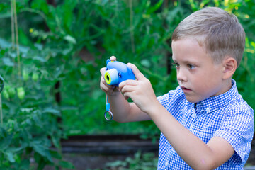A cute preschooler boy with a neat haircut in a blue shirt takes pictures of green plants in a greenhouse on a hot summer day. Selective focus. Portrait