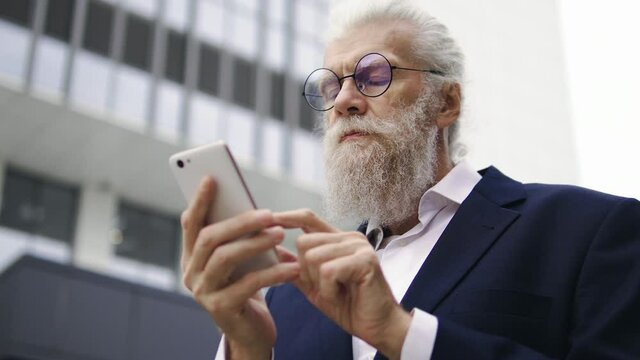 Serious elderly businessman looking through document pages in smartphone app