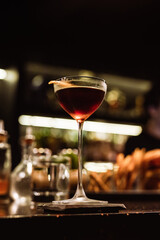 A classic Manhattan cocktail garnished with an orange zest in a beautiful glass at the bar